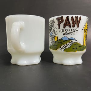 May include: Two white ceramic mugs with a cartoon illustration of a house and the text "Paw Yer Coffee's Ready!! Florida".