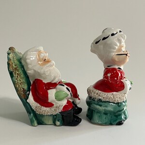 K&ouml;nnte beinhalten: Ein vintage Keramik-Salz- und Pfefferstreuer-Set mit Weihnachtsmann und Frau Claus. Der Weihnachtsmann sitzt auf einem gr&uuml;nen Stuhl mit wei&szlig;em Rand und h&auml;lt ein gr&uuml;nes und wei&szlig;es Geschenk. Frau Claus sitzt auf einem gr&uuml;nen Stuhl mit wei&szlig;em Rand und h&auml;lt ein gr&uuml;nes und wei&szlig;es Geschenk.