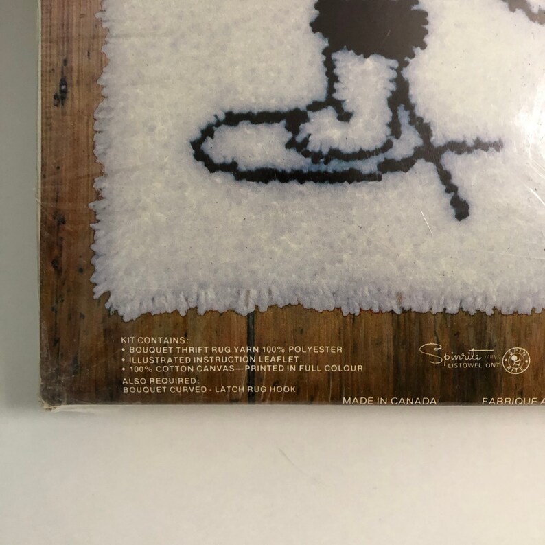 May include: A close-up of the back of a latch hook rug kit featuring a black and white outline of a snowman. The kit contains 100% polyester rug yarn, an illustrated instruction leaflet, and 100% cotton canvas printed in full color. The kit also requires a latch rug hook. The kit is made in Canada.