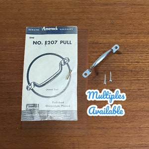 May include: A vintage Amerock cabinet pull, model number E207, in polished chrome. The pull is shown in a close-up image with two screws. The packaging includes the text "Genuine Amerock Hardware" and "Polished Chromium Plated".