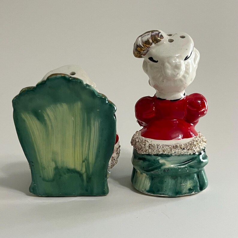K&ouml;nnte beinhalten: Vintage Salz- und Pfefferstreuer aus Keramik mit einer Frau in einem roten Kleid und einem gr&uuml;nen Stuhl. Die Frau hat ein wei&szlig;es Gesicht und goldenes Haar. Der Stuhl ist gr&uuml;n mit einem gelb-gr&uuml;nen Anstrich.