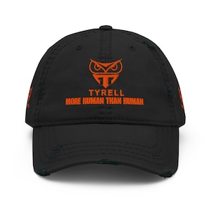 May include: Black distressed baseball cap with orange embroidered text and logo. The text reads "TYRELL MORE HUMAN THAN HUMAN" below an owl-like logo. The cap has a pre-worn look with distressed edges.