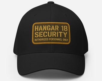 Puede incluir: Gorra de béisbol negra con un parche rectangular que dice "HANGAR 18 SECURITY AUTHORIZED PERSONNEL ONLY" en letras doradas. El parche tiene un borde dorado y un fondo verde oscuro. La gorra está hecha de un material suave.