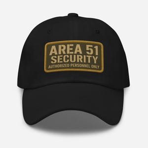 Puede incluir: Gorra de béisbol negra con un parche rectangular que dice "AREA 51 SECURITY AUTHORIZED PERSONNEL ONLY" en beige y verde oliva. La gorra tiene una visera curva y un botón en la parte superior.