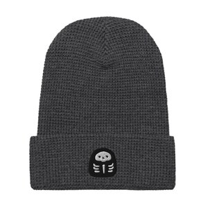 May include: A dark grey knitted beanie with a small embroidered skeleton design in white on the front.