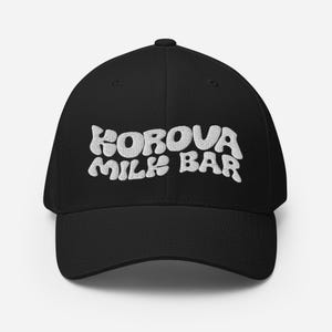 May include: Black baseball cap with white embroidered text that reads "Korova Milk Bar".