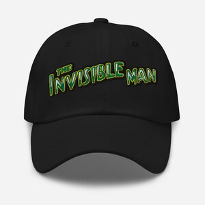 Op de afbeelding: Een zwarte baseballpet met de geborduurde tekst THE INVISIBLE MAN in een gestileerd lettertype met een groen en geel kleurverloop en een zwarte omlijning, gecentreerd op het voorpaneel van de pet met een gebogen klep en een knoop bovenop.