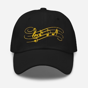 May include: Black baseball cap with embroidered gold musical notes, including a treble clef and musical notes on a staff. The cap has a curved brim and a structured crown.