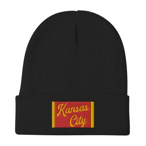 May include: Black knit beanie with a red and yellow embroidered patch that says "Kansas City".