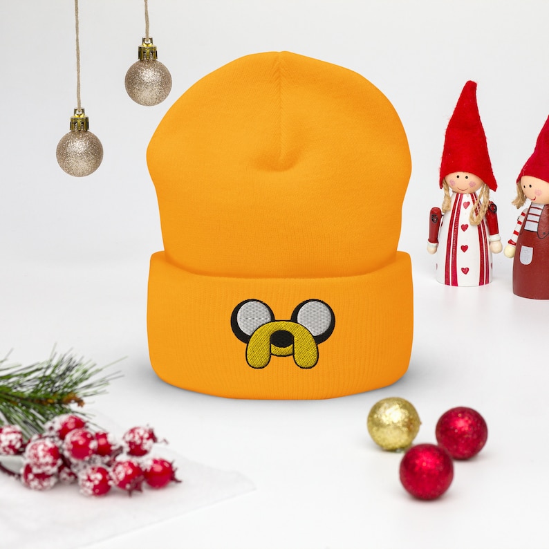 May include: A bright orange beanie with a black and white embroidered cartoon dog face. The beanie has a fold-over cuff.