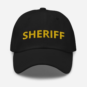 May include: A black baseball cap with the word "SHERIFF" embroidered in yellow.