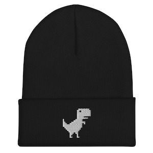 May include: Black knit beanie with a white pixelated dinosaur graphic. The dinosaur is a classic video game character.