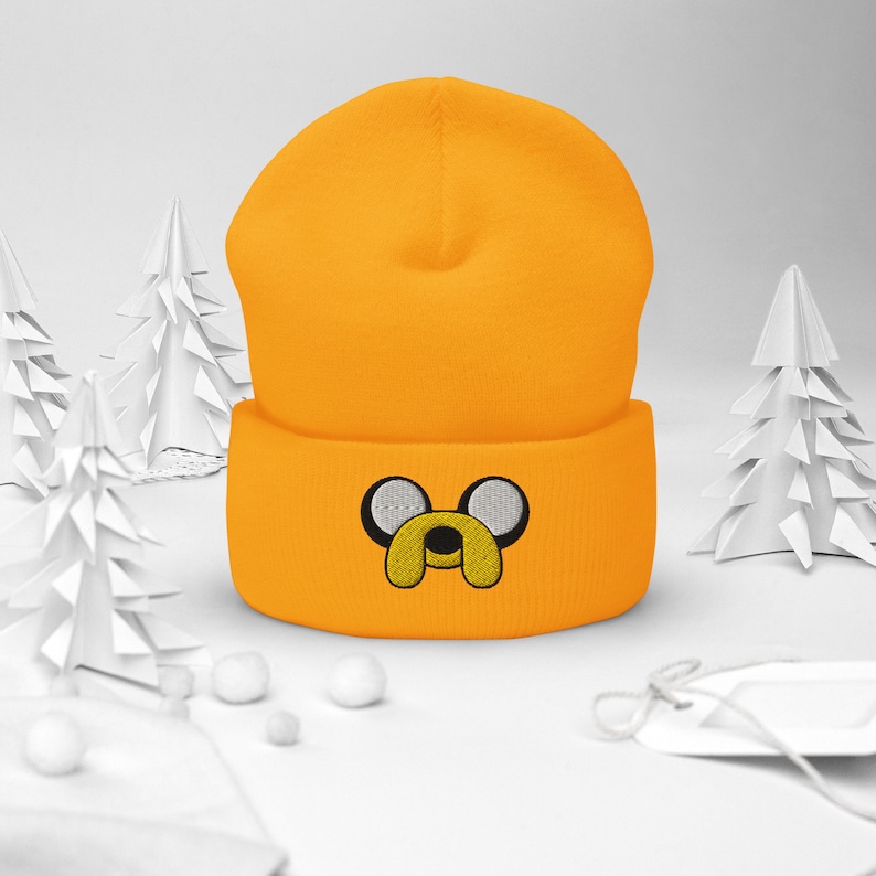May include: A bright yellow beanie with a cartoon dog face embroidered on the front. The dog has white eyes and a yellow nose.
