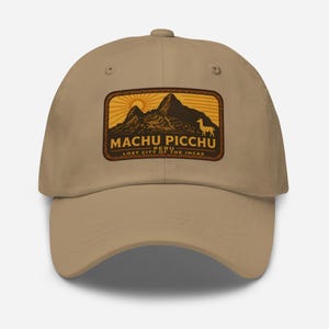 May include: A tan baseball cap featuring a rectangular patch with the words "Machu Picchu Peru, Lost City of the Incas." The patch depicts a mountain range, sun, and a llama in shades of brown and orange.