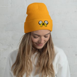May include: A yellow beanie with a black and white embroidered cartoon dog face. The dog has large eyes and a small nose.