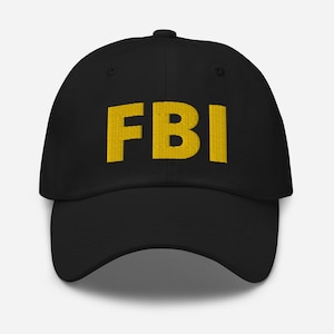 Puede incluir: Una gorra de béisbol negra con un logotipo "FBI" bordado en amarillo.