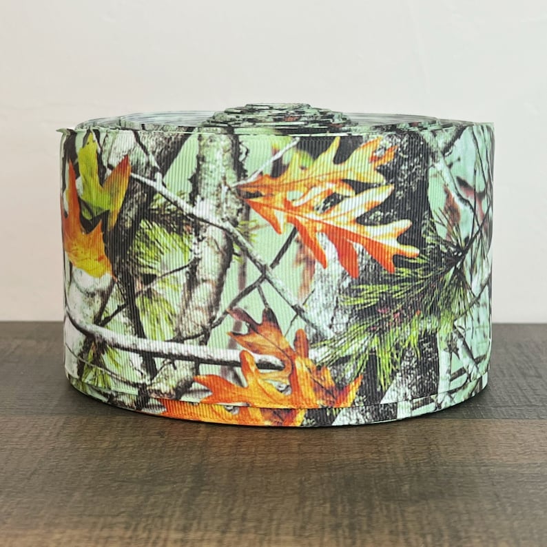 May include: A roll of green, brown, and orange camouflage ribbon with a leaf pattern.