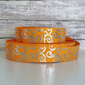 May include: Orange and silver ribbon with a swirling pattern. The ribbon is folded in half and the silver pattern is visible on both sides.