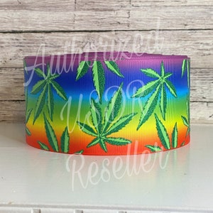 May include: Rainbow colored ribbon with a green marijuana leaf pattern. The ribbon is made of a shiny material and has a slight glitter effect.
