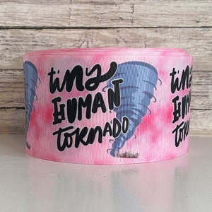 May include: A roll of pink ribbon with the words "tiny HUMAN tornado" in black script. A blue and gray tornado graphic is on the ribbon. The background has a pink tie-dye effect.