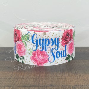 May include: White ribbon with a floral pattern and gold glitter. The ribbon has the words "Gypsy Soul" printed in blue.