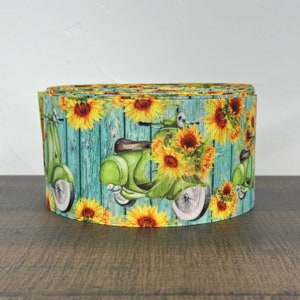 May include: Green and yellow ribbon with a repeating pattern of a vintage scooter and sunflowers on a blue wood background.