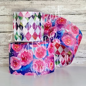 May include: Two rolls of pink and white ribbon with a watercolor floral and diamond pattern. The floral pattern features pink roses on a blue and white background. The diamond pattern is white with pink and green accents.