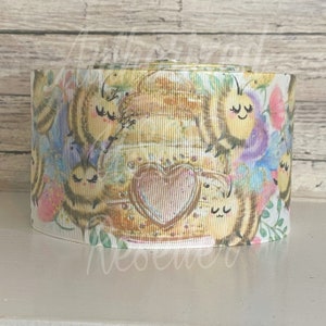 May include: A roll of decorative ribbon featuring a watercolor design of bees, hearts, and flowers. The ribbon has a white background with a repeating pattern of bees in various poses, surrounded by floral elements in pastel colors.