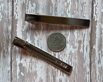 Può includere: Due fermagli per capelli argentati, uno con superficie testurizzata e l'altro liscio, sono mostrati su una superficie di legno. Una moneta da 25 centesimi di dollaro americano è inclusa come riferimento per le dimensioni.