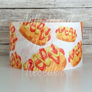 May include: White ribbon with a repeating pattern of hot dogs with mustard and ketchup. The hot dogs are illustrated in a cartoon style.