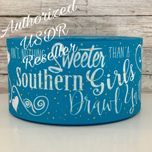 May include: Turquoise blue ribbon with gold glitter and white text that reads "Ain't nothing sweeter than a Southern Girls Drawl Y'all". The ribbon is a craft supply for making bows and hair accessories.