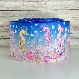 May include: A blue and white ribbon with a seahorse and coral reef design. The ribbon features pink, yellow, and brown seahorses, coral, and seashells.