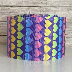 May include: A roll of purple ribbon with a rainbow heart pattern. The hearts are arranged in rows and are a gradient of colors, including red, orange, yellow, green, blue, and purple.