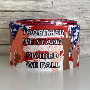 May include: Red, white, and blue ribbon with an American flag design and the words "Together We Stand Divided We Fall". The ribbon features illustrations of hands of different skin tones holding each other.