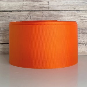 May include: A roll of bright orange ribbon. The ribbon is a solid color and has a slight sheen.