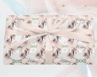 Pode incluir: Uma caixa de presente branca com uma fita rosa e um padrão floral com um casal. A caixa está embrulhada em papel que diz "Wedding" várias vezes.