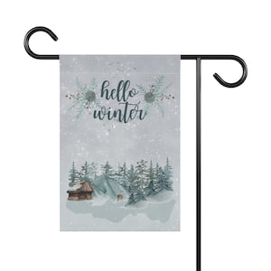 May include: A winter-themed garden flag with a snowy scene featuring a cabin, trees, and a deer. The flag has the text "hello winter" in a blue-green font.