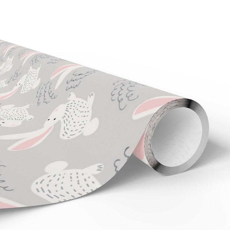 May include: A gray and white wrapping paper with a repeating pattern of pink-eared bunnies hopping on clouds. The bunnies are white with black dotted outlines and the clouds are gray with white outlines.