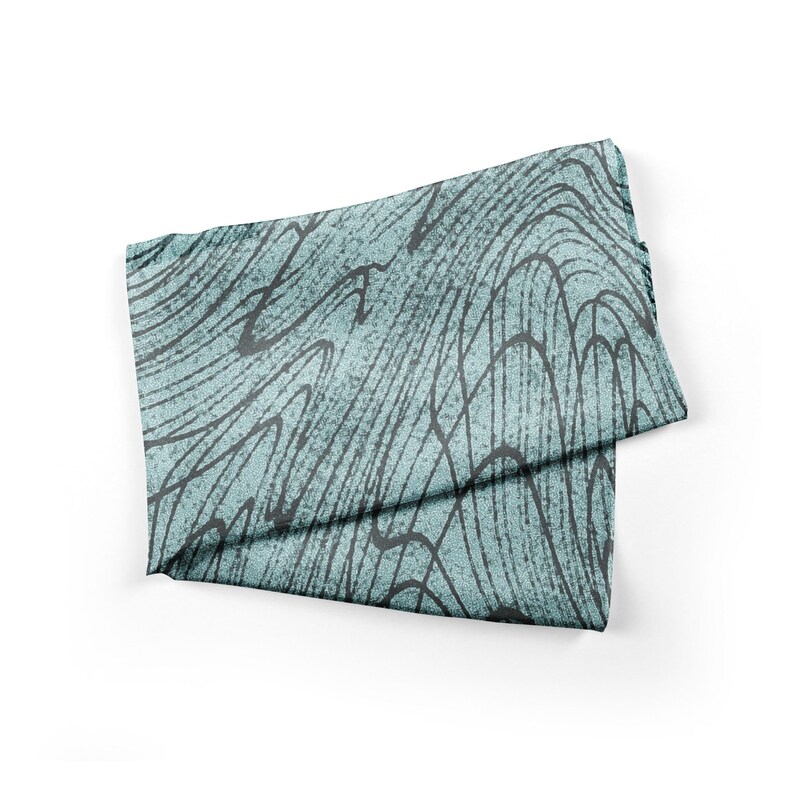 May include: A folded teal blue fabric with a black and white abstract pattern. The fabric has a soft, textured surface.