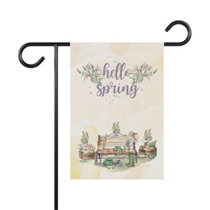 May include: A garden flag with a watercolor design featuring a bench, flowers, gardening tools, and butterflies. The text "hello spring" is written in purple on the flag.