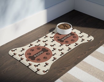 May include: A beige dog food mat with a brown dachshund pattern. The mat has two circles with the words "FOOD" and "WATER" printed on them. A white bowl with dog food is on the mat.
