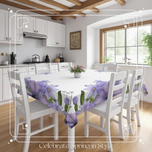 Peut inclure: Table de salle &agrave; manger blanche avec six chaises blanches, recouverte d'une nappe blanche &agrave; motif floral violet. Le texte "Celebrate Spring in Style" est en bas de l'image.