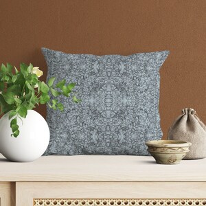 May include: A light blue throw pillow with a geometric pattern. The pillow is sitting on a light wood table with a woven basket underneath.