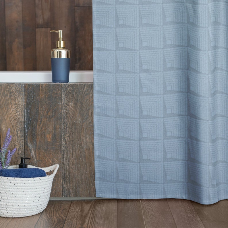 May include: A blue shower curtain with a geometric pattern hangs in a bathroom. A gold and blue soap dispenser sits on the edge of a white bathtub.
