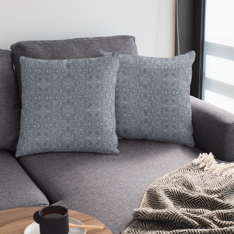 May include: Two gray throw pillows with a textured fabric on a gray couch with a black and white throw blanket.