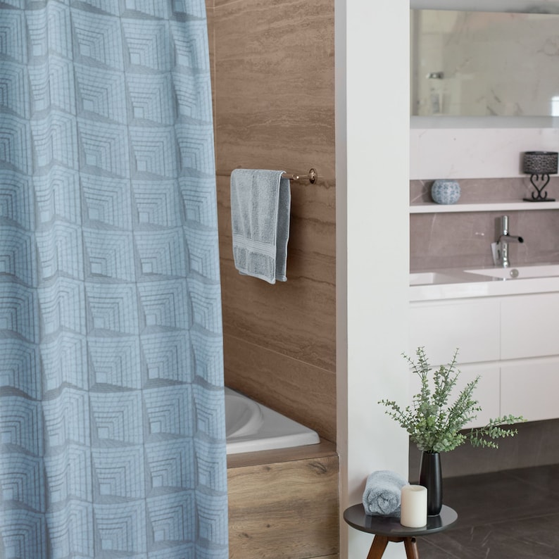 May include: A light blue shower curtain with a geometric pattern hangs in a bathroom with a white bathtub, a towel rack with a towel, and a small table with a plant and a candle.