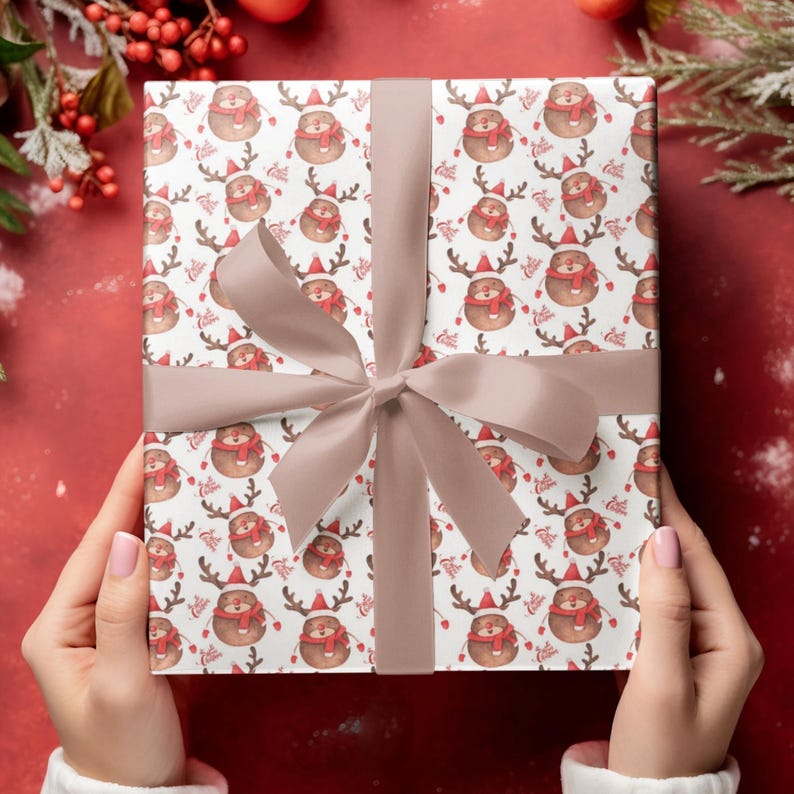 Op de afbeelding: Een ingepakt cadeau met een feestelijk rendierpatroon op wit papier. De rendieren dragen rode sjaals en mutsen. Een lichtbruin lint is om het cadeau gebonden. De achtergrond is effen rood met decoratieve elementen.