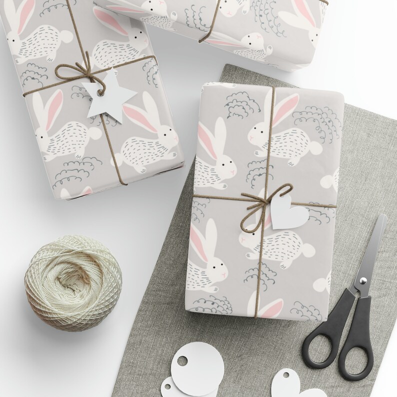 May include: Three gift boxes wrapped in gray wrapping paper with a white bunny rabbit pattern. The boxes are tied with brown twine and have white paper tags attached.