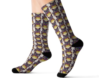 May include: A pair of white socks with a repeating pattern of cartoon cats with purple, yellow, and orange colors. The socks are black at the toes and heels.