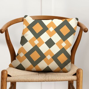 May include: A throw pillow with a geometric pattern featuring orange and gray squares on a cream background.